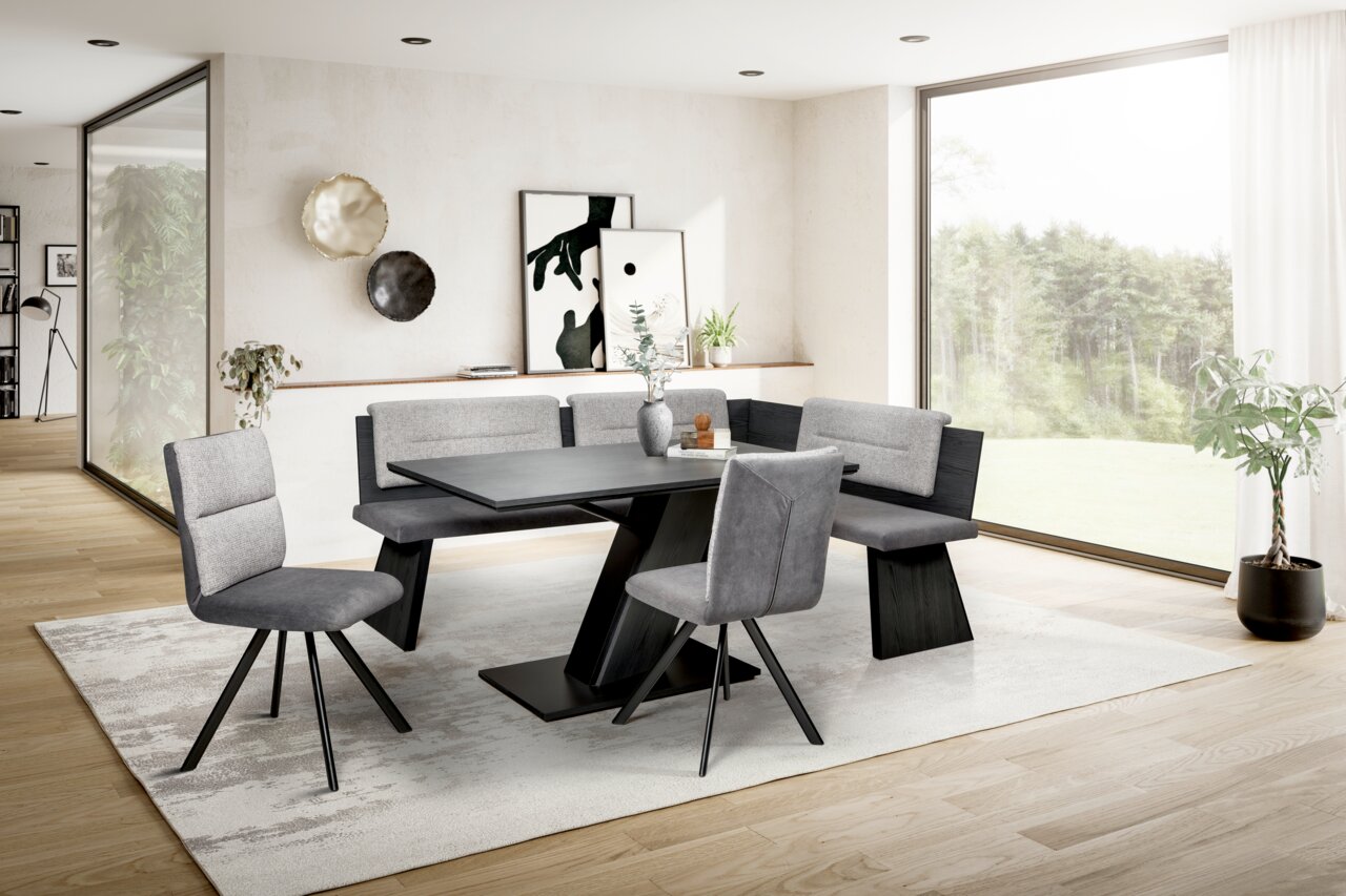 Moderne Eckbankgruppe in einem hellen Wohnzimmer mit großen Fenstern, bestehend aus einem Tisch, einer Eckbank und zwei Stühlen in grauen Tönen, seitliche Perspektive.