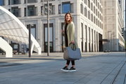 Een vrouw in de stad met een grijze boodschappentas, die een kopje koffie vasthoudt. Vooraanzicht.
