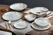 Tafelservice 18-tlg. mit dekorativem Muster, bestehend aus Tellern und Schalen, auf einem Holztisch arrangiert, seitliche Perspektive