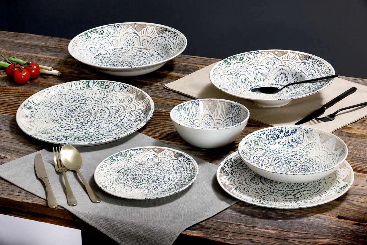 Tafelservice 18-tlg. mit dekorativem Muster, bestehend aus Tellern und Schalen, auf einem Holztisch arrangiert, seitliche Perspektive