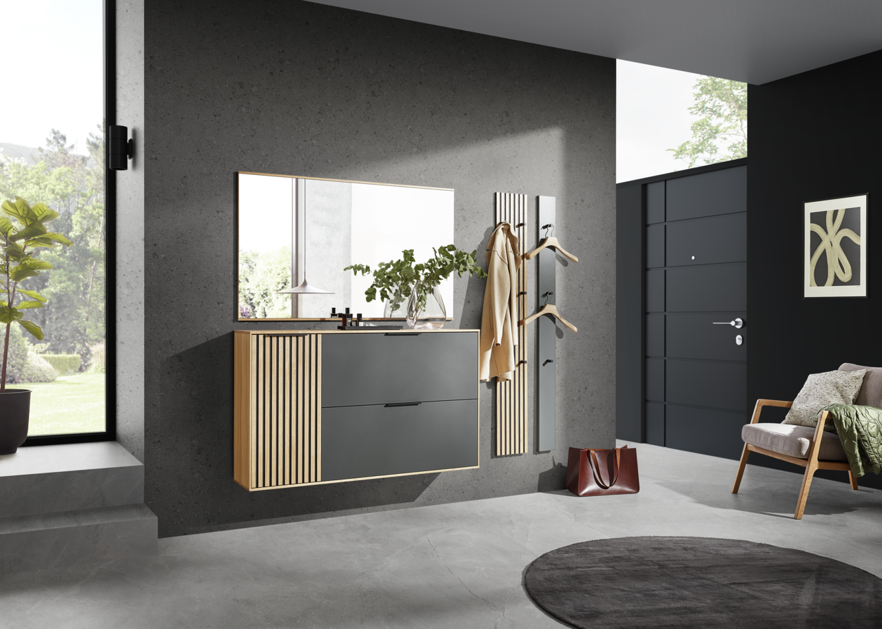 Moderner Eingangsbereich mit hängendem Schuhschrank, großem Spiegel und Garderobenpaneel in Holzoptik. Perspektive von schräg vorne.