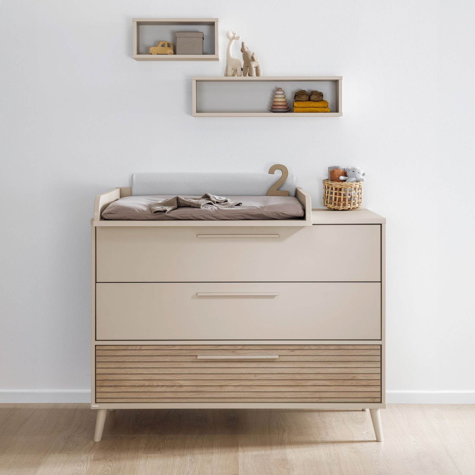 Breite Kommode mit drei Schubladen, obere Schublade mit Wickelauflage, dekoriert mit Spielzeug und Körbchen, Frontalansicht