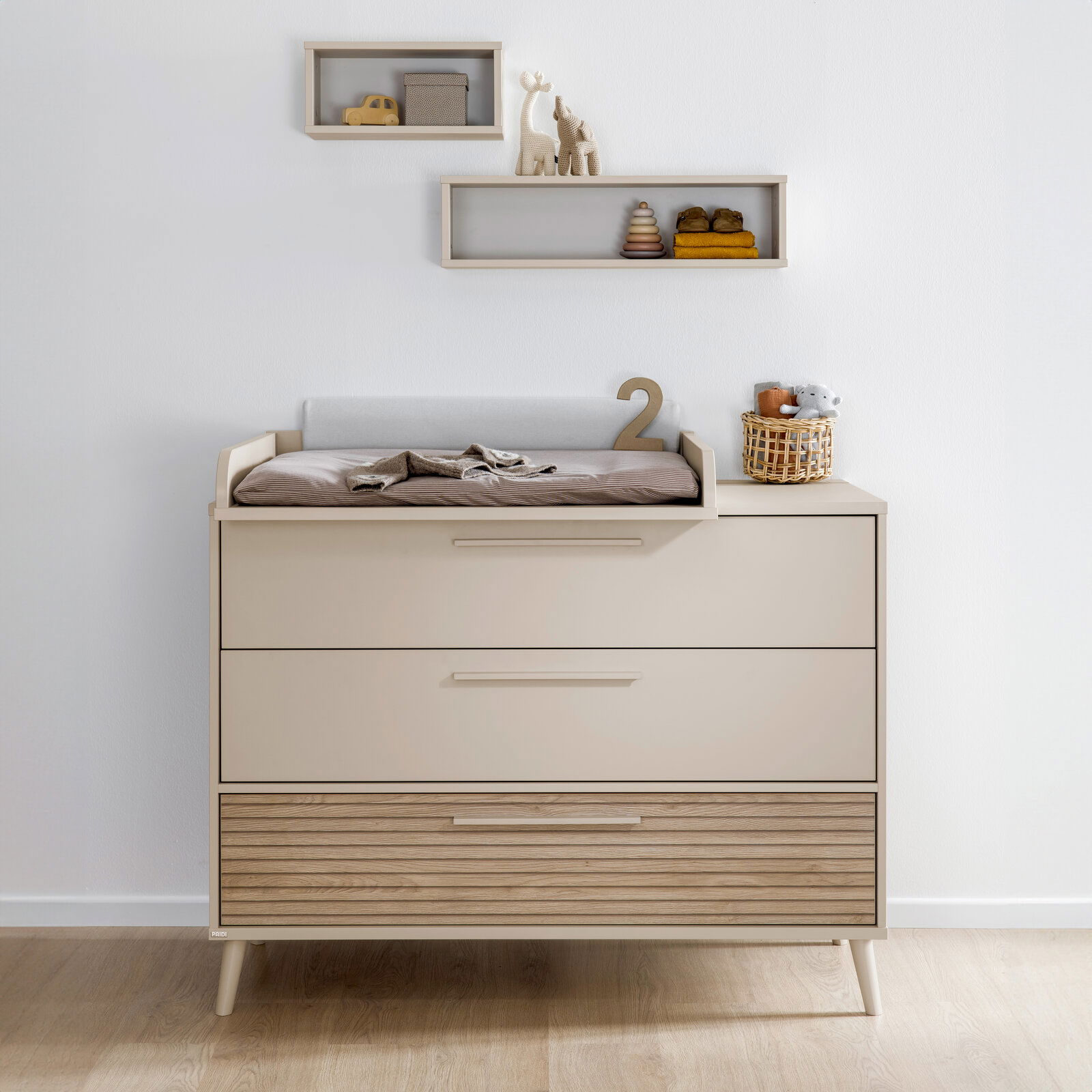 Breite Kommode mit drei Schubladen, obere Schublade mit Wickelauflage, dekoriert mit Spielzeug und Körbchen, Frontalansicht