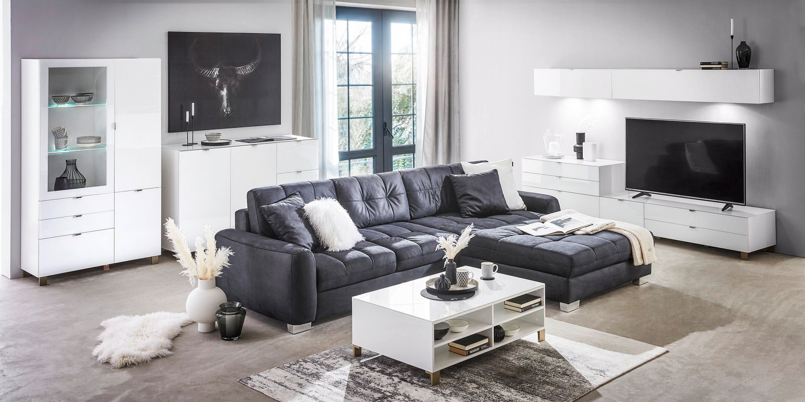 Modernes Wohnzimmer mit weißem Sideboard, Vitrine und Couchtisch, grauem Sofa und Wandregal, seitliche Perspektive