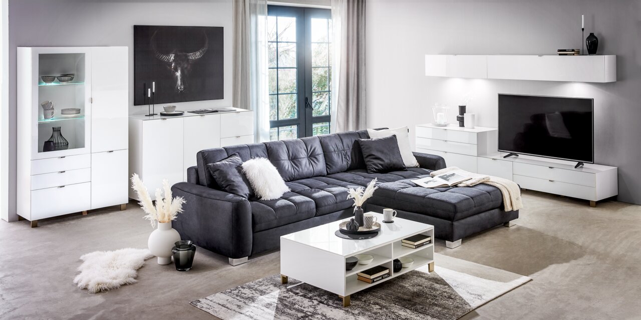 Modernes Wohnzimmer mit weißem Sideboard, Vitrine und Couchtisch, grauem Sofa und Wandregal, seitliche Perspektive