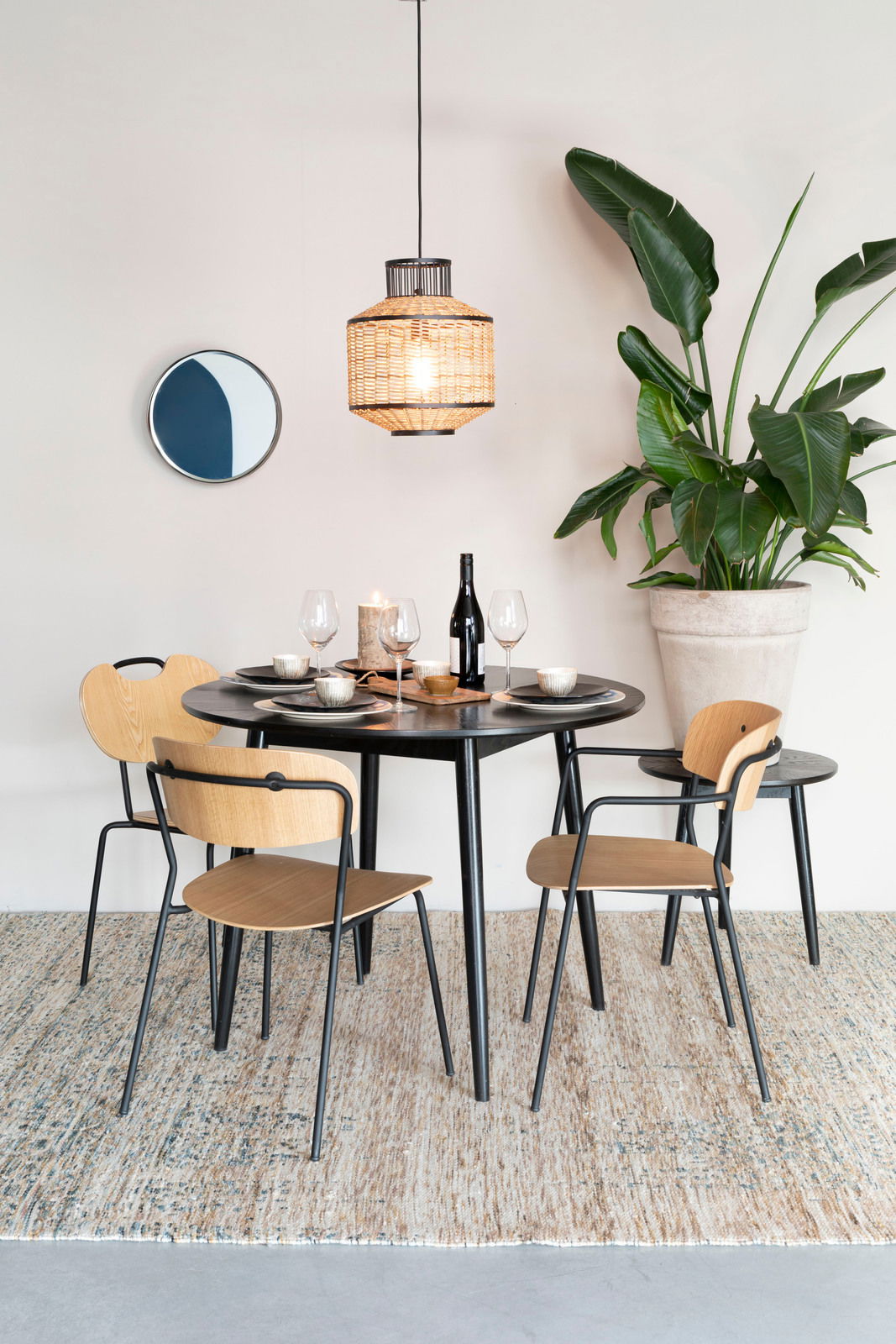 Esszimmer mit modernem Stuhl-Set aus Holz und Metall, runder Tisch, hängende Lampe und große Pflanze, seitliche Perspektive