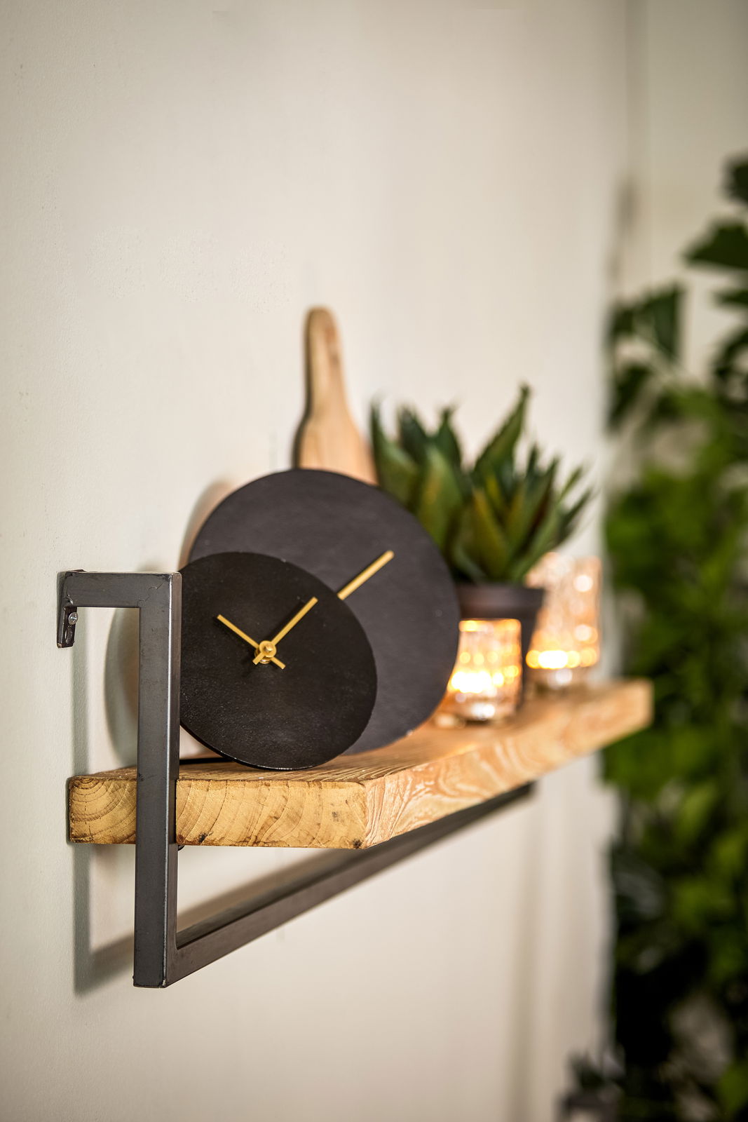 Moderne schwarze Wanduhr mit goldenen Zeigern auf einem Holzregal, seitliche Perspektive
