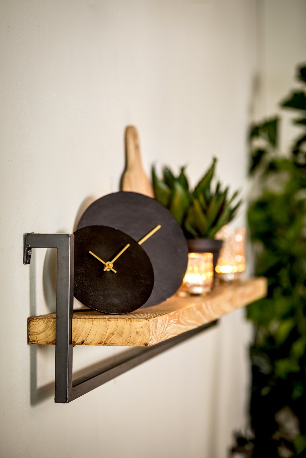 Moderne zwarte wandklok met gouden wijzers op een houten plank, zijaanzicht