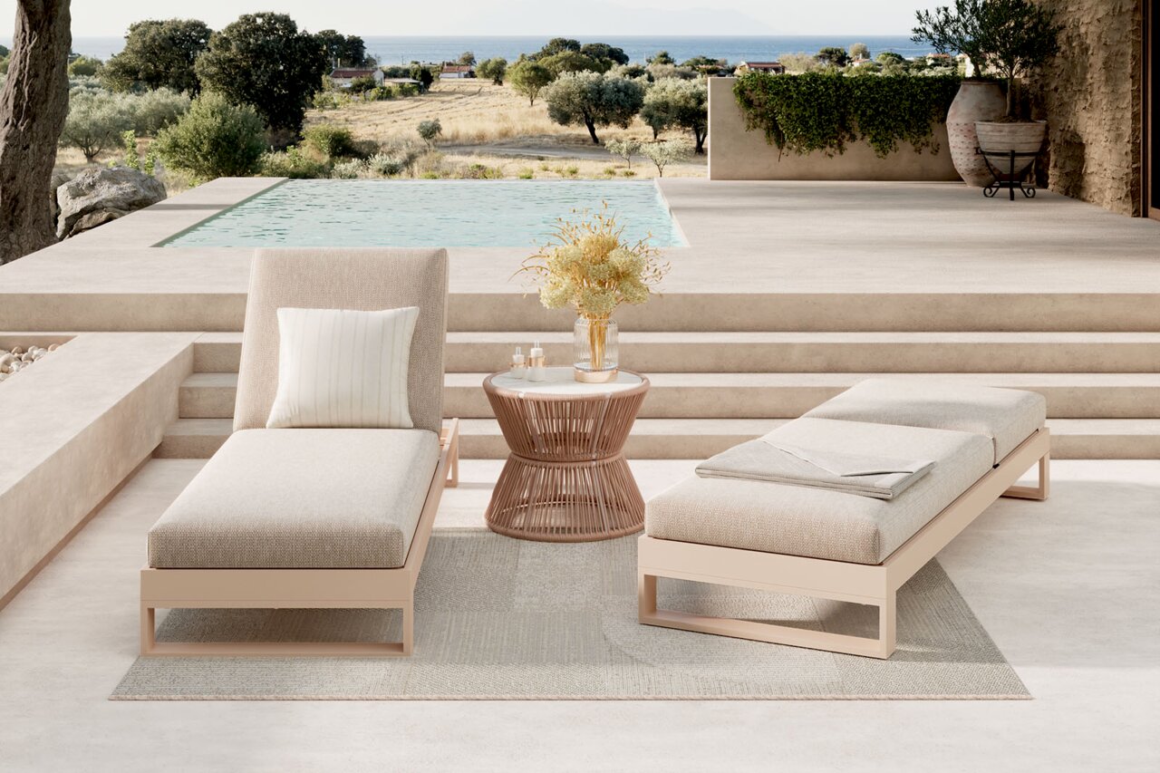 Amatio Sonnenliege WILLIS Zwei moderne Outdoor-Liegen in Beige mit Kissen und Decke neben einem runden Beistelltisch auf einer Terrasse am Pool, Blick aus frontaler Perspektive auf die Sitzgruppe mit Landschaft und Meer im Hintergrund