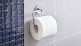 Toilettenpapierrolle auf einem modernen, verchromten Halter an einer Badezimmerwand, seitliche Perspektive
