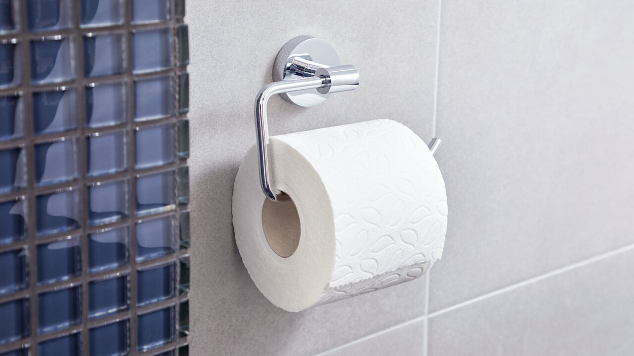 Toilettenpapierrolle auf einem modernen, verchromten Halter an einer Badezimmerwand, seitliche Perspektive
