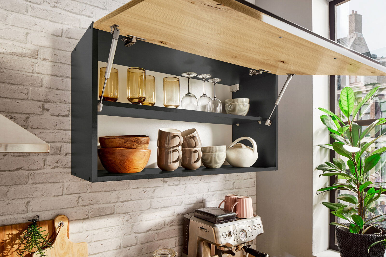 Küchenblock mit geöffnetem Hängeschrank, gefüllt mit Gläsern, Tassen und Schalen, aus seitlicher Perspektive fotografiert.