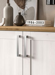 Nahaufnahme einer modernen Kommode mit hellen Holztüren und silbernen Griffen, dekoriert mit Vasen und Büchern auf der Oberseite.
