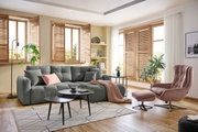 Gemütliche Wohnzimmer-Ecke mit grauem Rundecksofa, dekoriert mit Kissen und Decke, im Vordergrund ein runder Couchtisch, seitliche Perspektive.