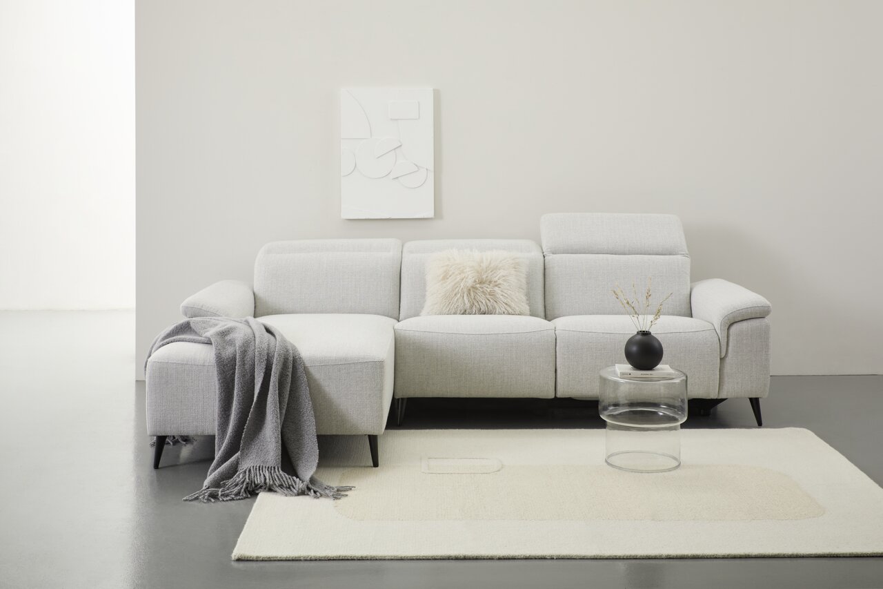 Graue Longchairkombination mit Kissen und Decke, frontal fotografiert, auf hellem Teppich mit rundem Glastisch und schwarzer Vase.