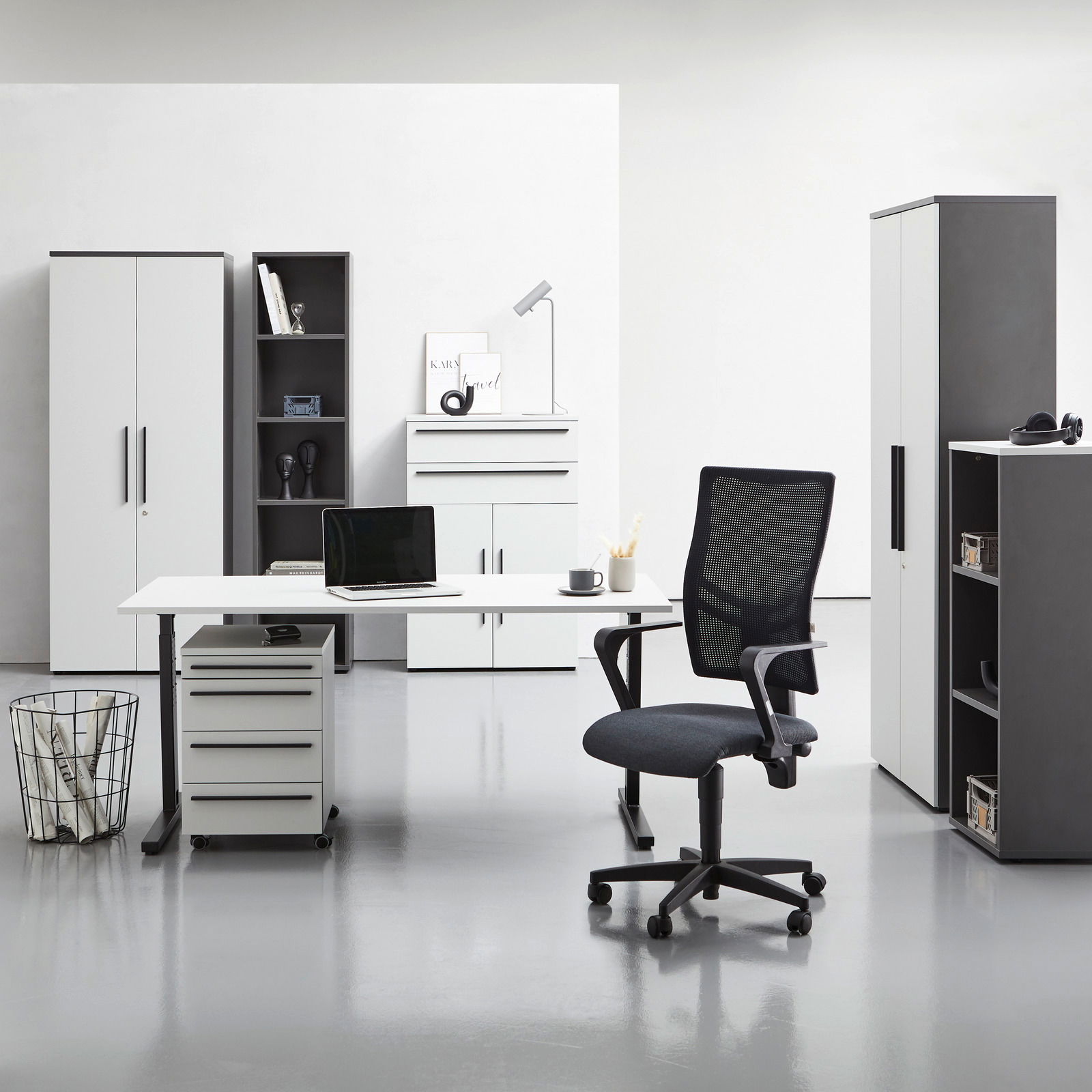 Moderne Büromöbel in einem hellen Raum, darunter ein Schreibtisch mit Rollcontainer, ein Bürostuhl und mehrere Aktenschränke. Frontalansicht.