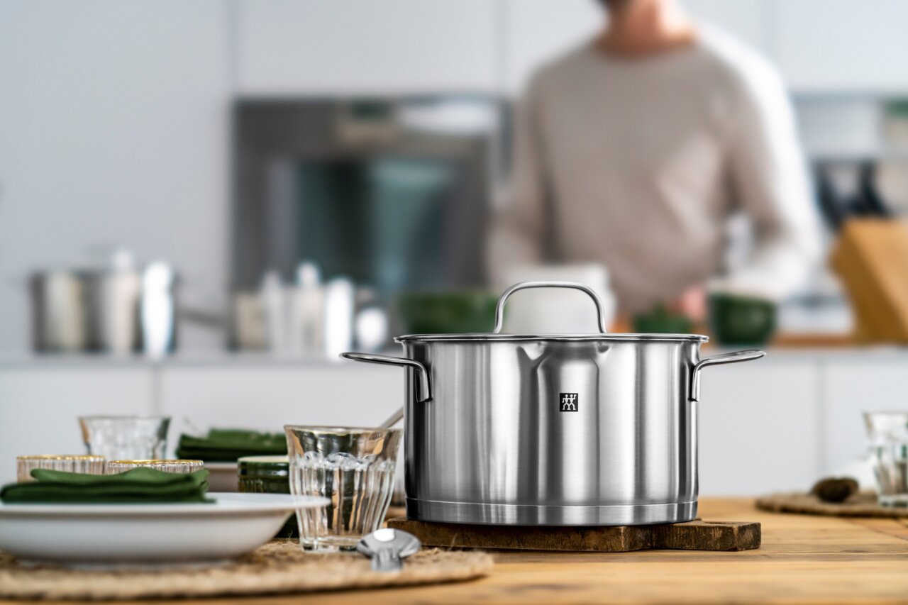 Roestvrijstalen kookpan uit de 5-delige pannenset True Flow, vooraan op een houten tafel in een moderne keuken geplaatst.