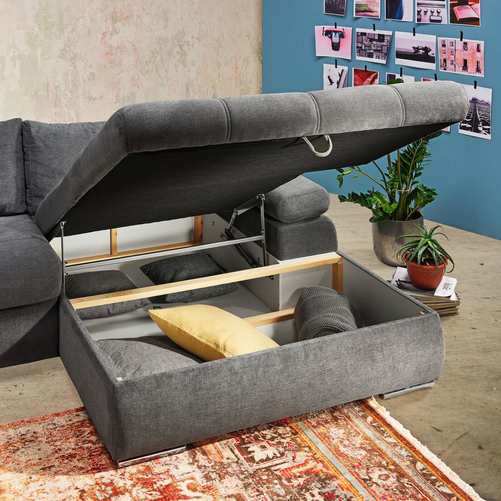 Graues Ecksofa mit aufklappbarem Stauraum, gefüllt mit Kissen, aus der Perspektive von oben rechts fotografiert.