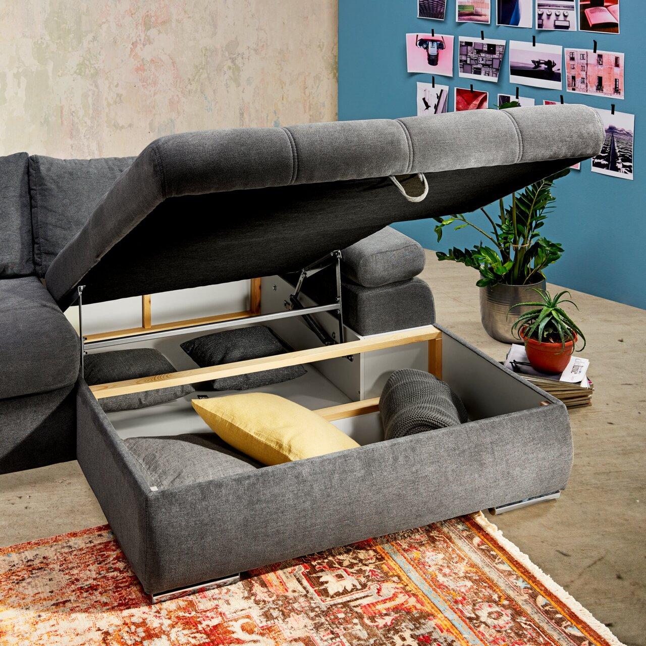 Graues Ecksofa mit aufklappbarem Stauraum, gefüllt mit Kissen, aus der Perspektive von oben rechts fotografiert.