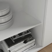 Nahaufnahme eines weißen Sideboards mit Regalfächern, gefüllt mit Büchern und runden Boxen, aus seitlicher Perspektive.