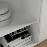 Nahaufnahme eines weißen Sideboards mit Regalfächern, gefüllt mit Büchern und runden Boxen, aus seitlicher Perspektive.