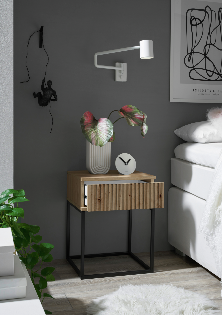 Moderne Nachtkommode aus Holz mit schwarzem Metallgestell, dekoriert mit einer Pflanze und einer Uhr, seitliche Perspektive.