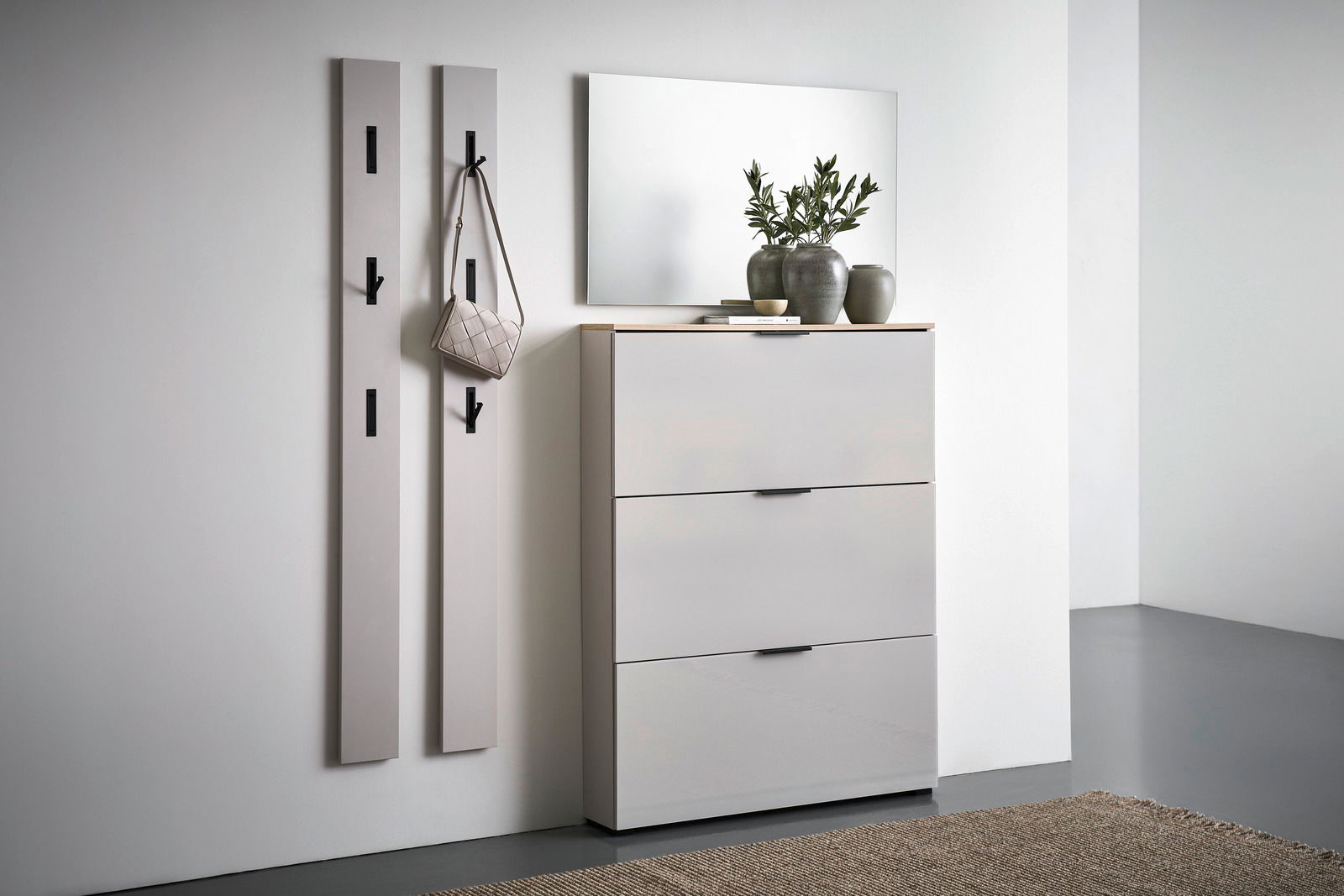 Voleo Klapp-Schuhschrank NEW YORK Moderne Garderobeneinrichtung mit zwei vertikalen Paneelen mit Haken, einem Spiegel und einem dreitürigen Schuhschrank in einer hellen, minimalistischen Umgebung. Perspektive von vorne rechts.