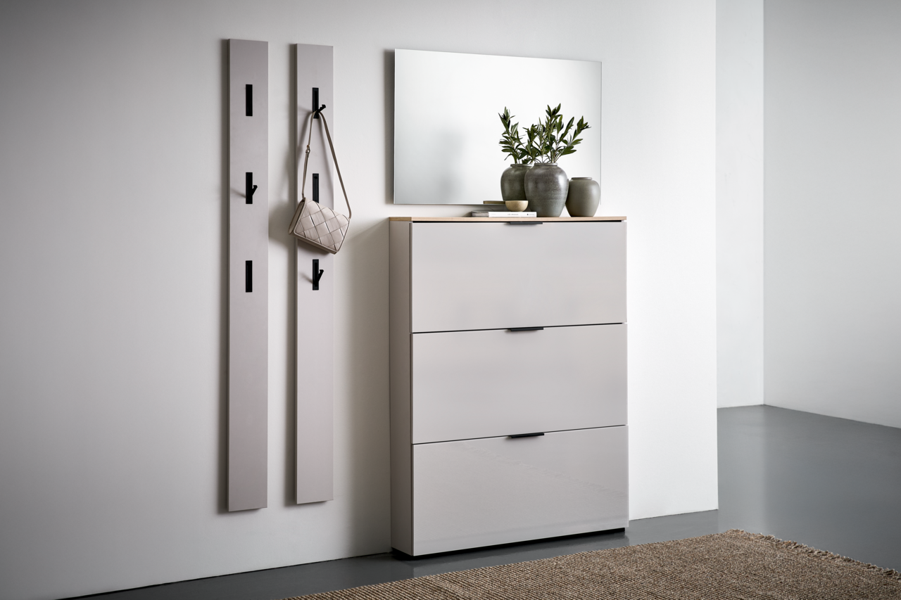 Voleo Klapp-Schuhschrank NEW YORK Moderne Garderobeneinrichtung mit zwei vertikalen Paneelen mit Haken, einem Spiegel und einem dreitürigen Schuhschrank in einer hellen, minimalistischen Umgebung. Perspektive von vorne rechts.