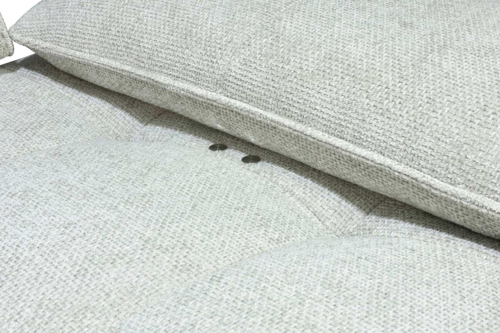 Nahaufnahme eines hellgrauen Longchairs mit strukturierter Stoffoberfläche und Knopfdetails, seitliche Perspektive.