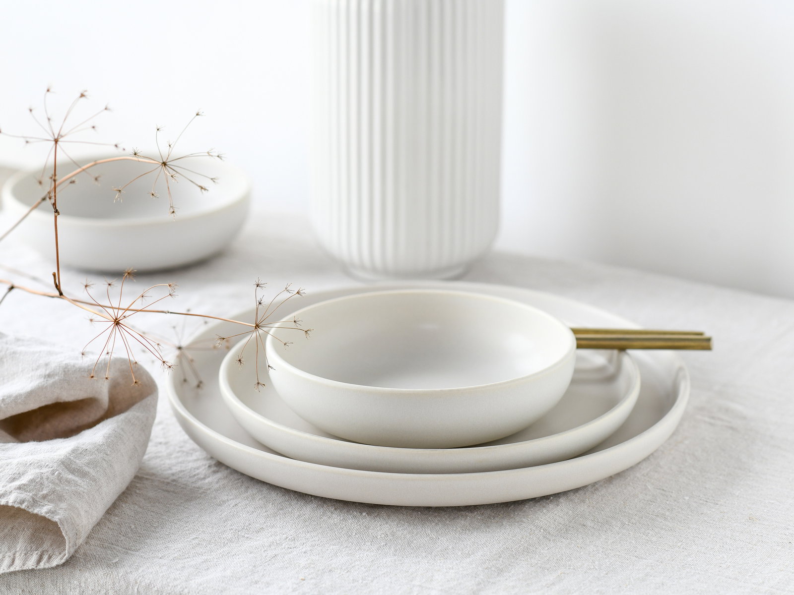Elegantes weißes Tellerset aus Keramik, bestehend aus drei Tellern in verschiedenen Größen, stilvoll arrangiert auf einem Tisch mit natürlichem Leinenstoff, seitliche Perspektive.