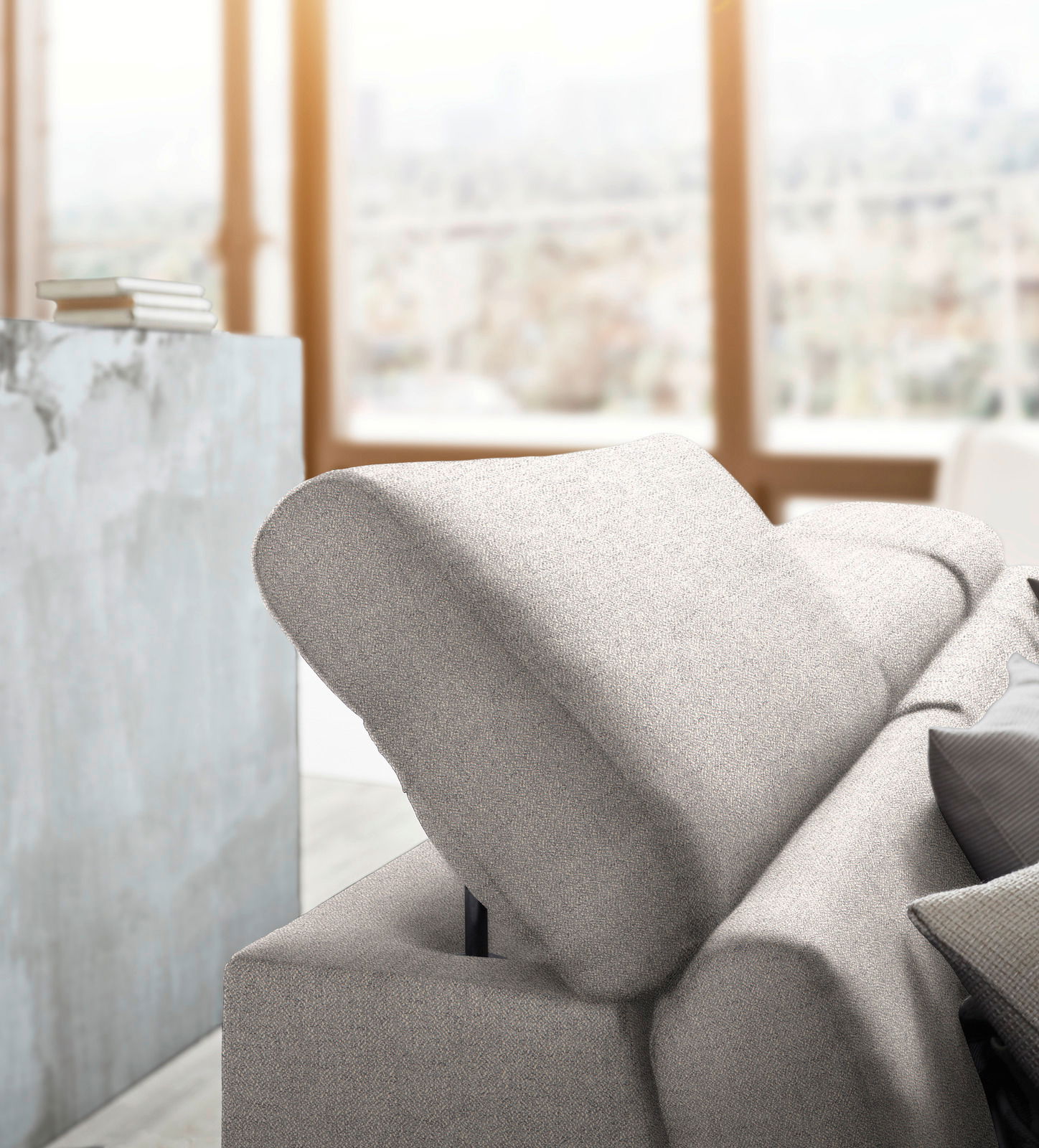 Nahaufnahme einer modernen, hellgrauen Rundecke mit verstellbarer Rückenlehne in einem hellen Raum mit großen Fenstern.