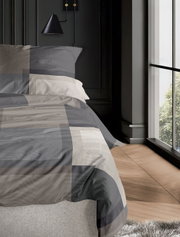 Bettwäsche-Set irisette WAVE in Grau- und Beigetönen, auf einem Bett in einem modernen Schlafzimmer mit Holzfußboden und großem Fenster, seitliche Perspektive.