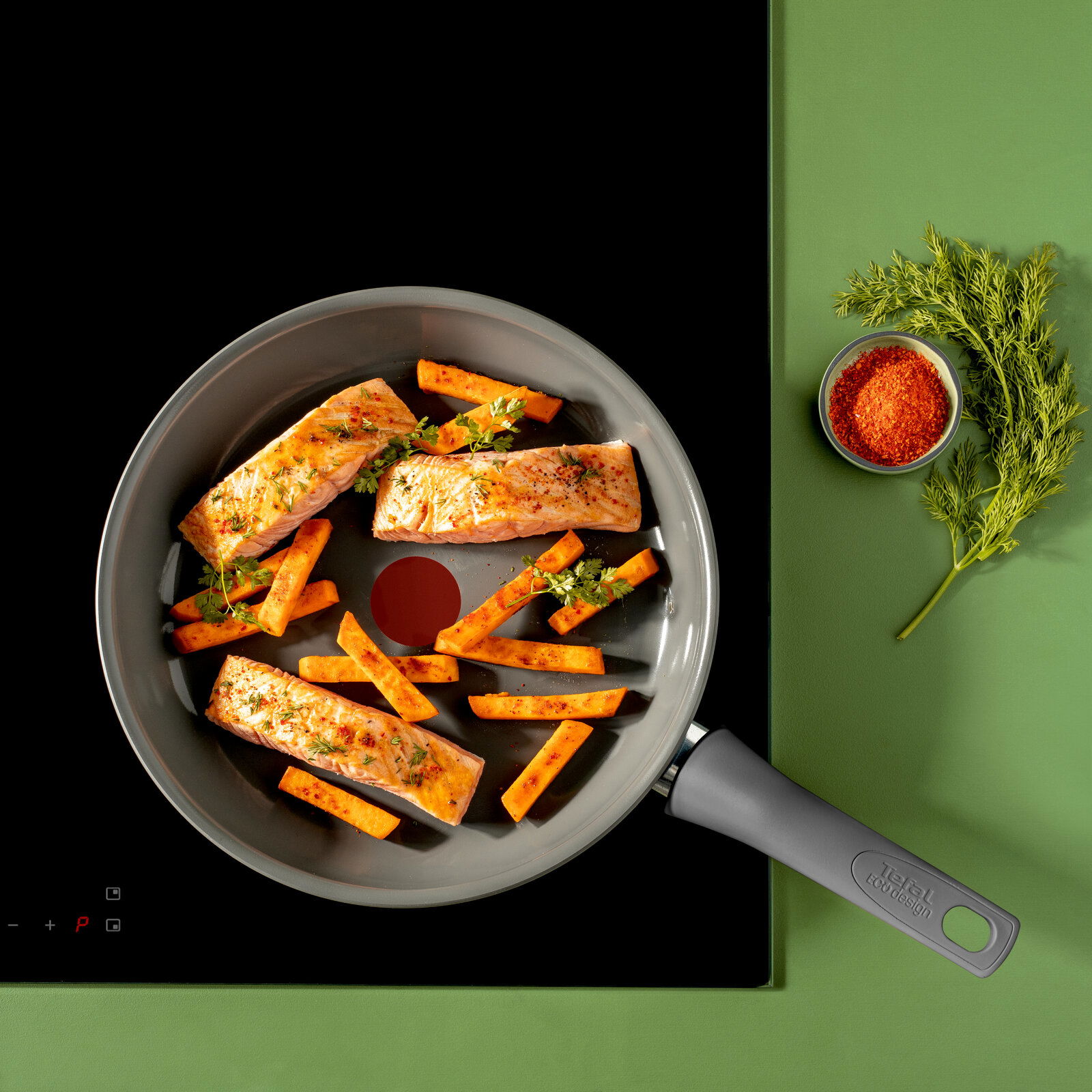Pfanne mit Lachsfilets und Karottenstiften, von oben fotografiert, auf einem Herd mit grünem Hintergrund.