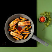 Pfanne mit Lachsfilets und Karottenstiften, von oben fotografiert, auf einem Herd mit grünem Hintergrund.
