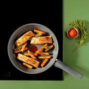 Pfanne mit Lachsfilets und Karottenstiften, von oben fotografiert, auf einem Herd mit grünem Hintergrund.