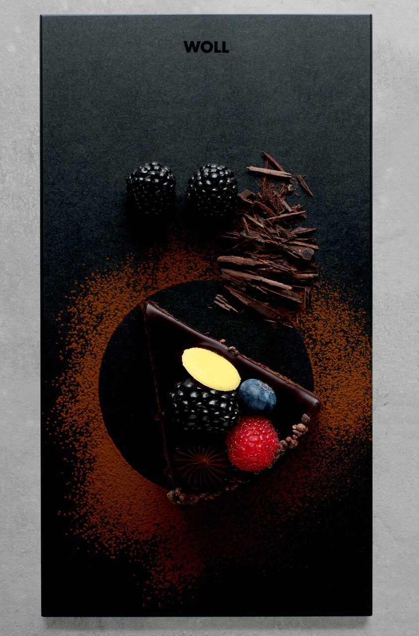 Vogelperspektive auf ein elegantes Frühstücksset mit einer Schieferplatte, dekoriert mit einem Stück Schokoladenkuchen, frischen Beeren und Schokoladenspänen.