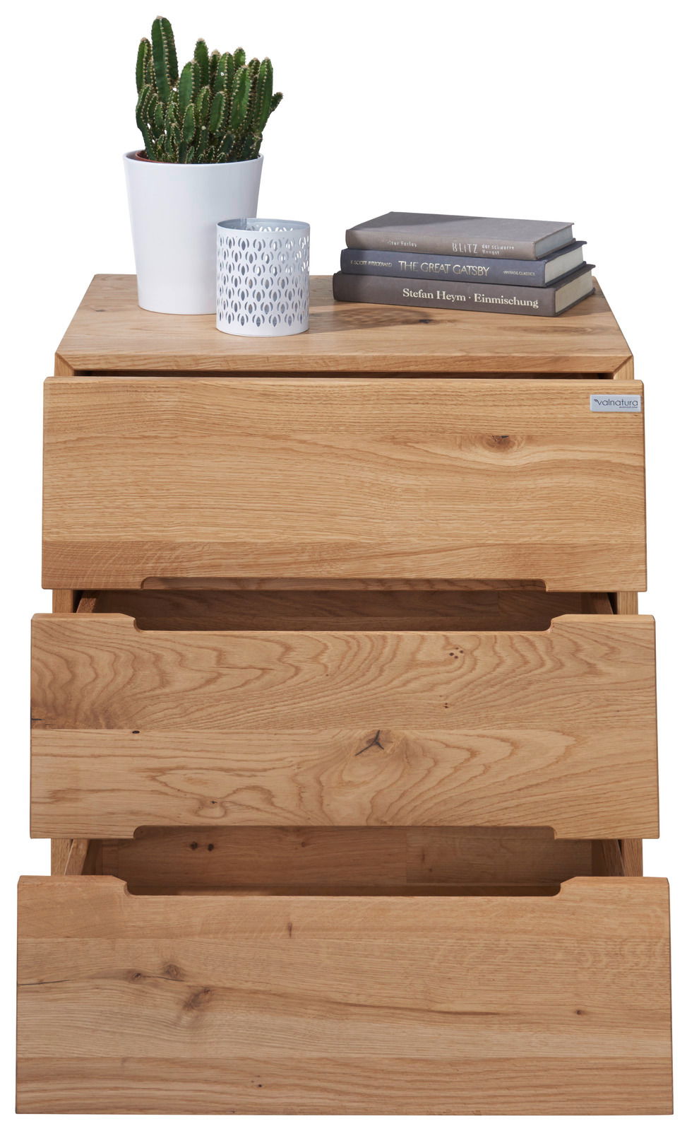 Nachtkonsole aus Holz mit drei Schubladen, darauf ein Kaktus in einem weißen Topf, eine dekorative Kerze und drei Bücher. Frontalansicht.