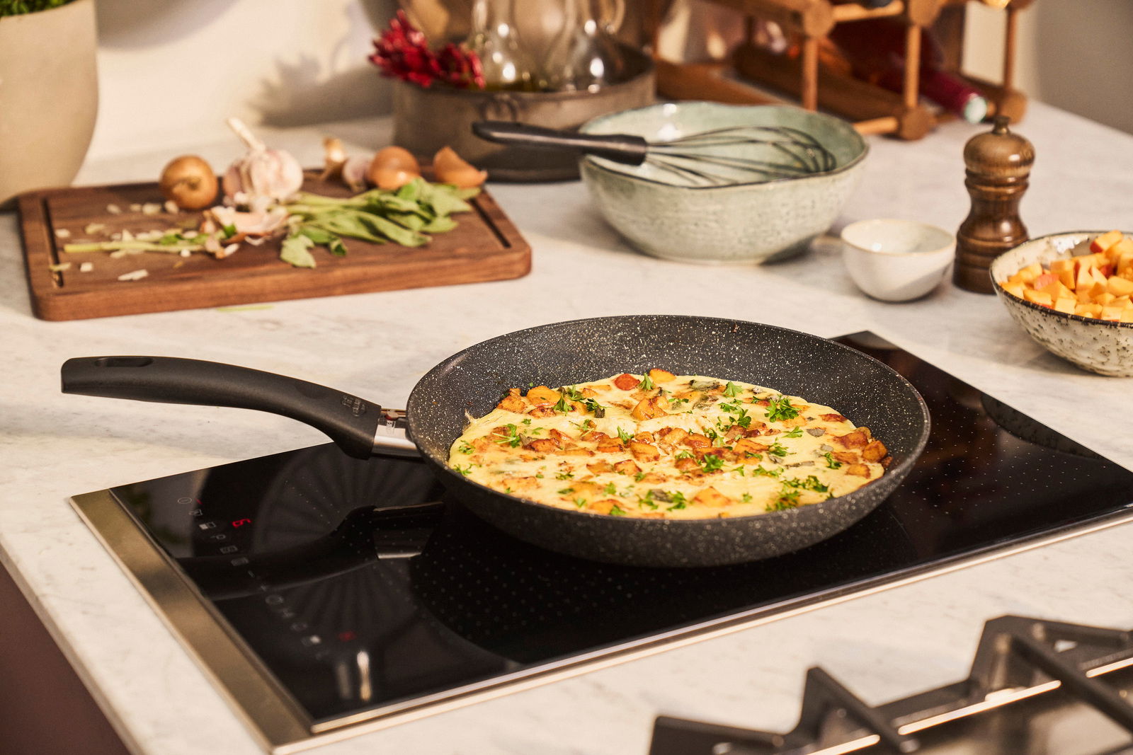 Bratpfanne mit 32 cm Durchmesser auf einem Herd, gefüllt mit einem Omelett, umgeben von Zutaten und Küchenutensilien, aus seitlicher Perspektive.