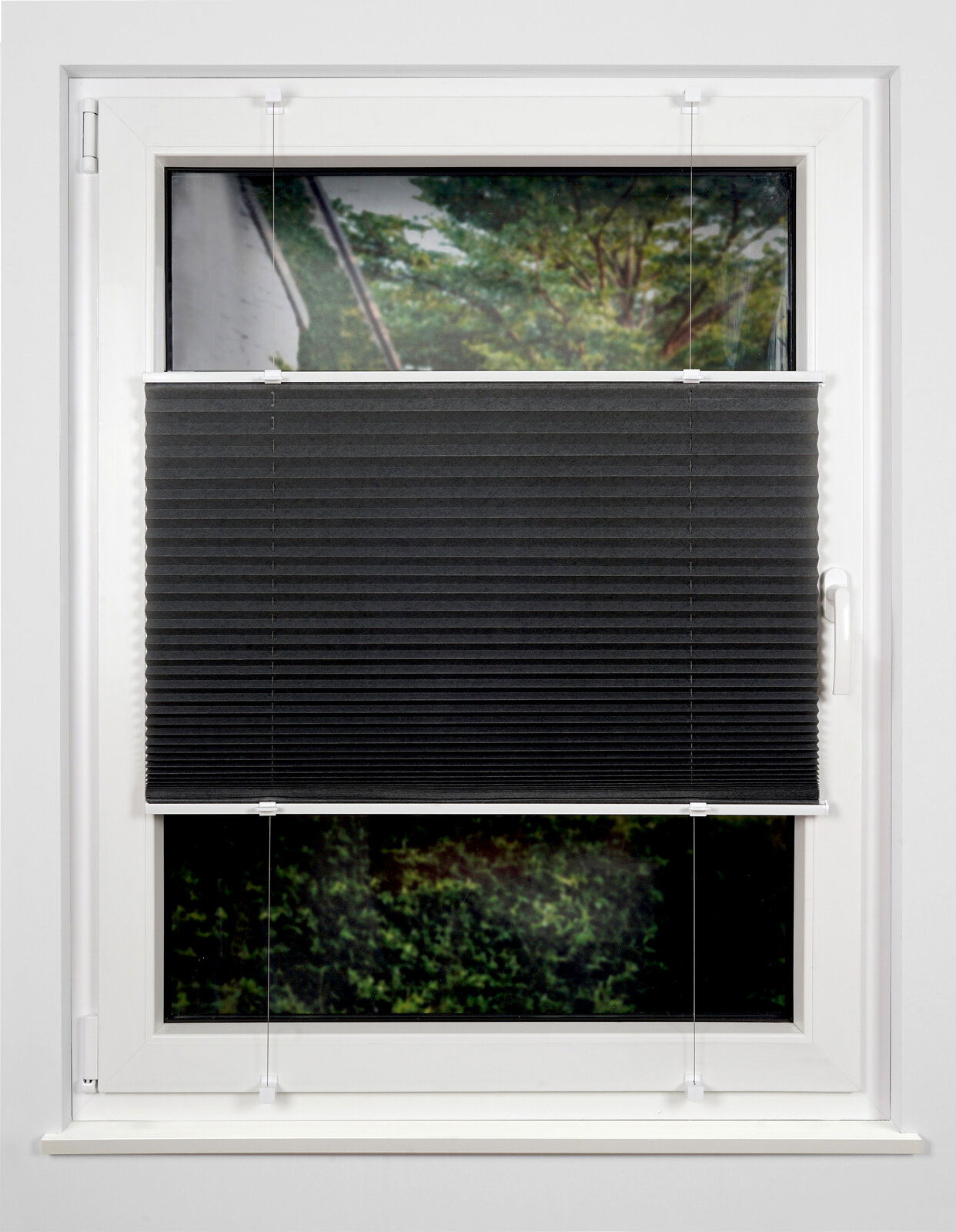 Schwarzes Plissee am Fenster, halb heruntergelassen, mit Blick auf einen Garten im Hintergrund.