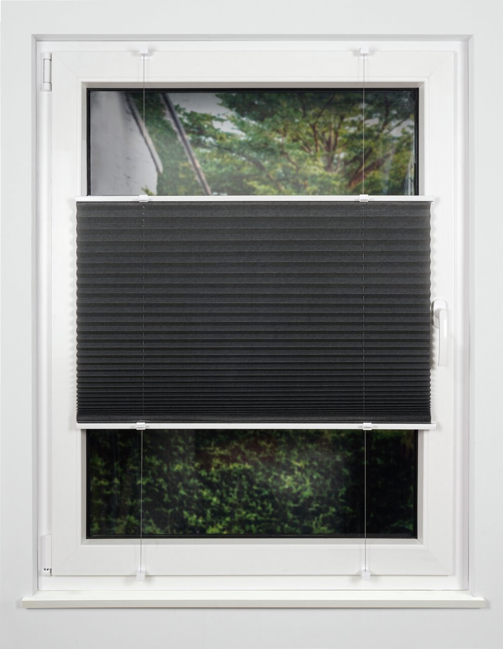 Schwarzes Plissee am Fenster, halb heruntergelassen, mit Blick auf einen Garten im Hintergrund.