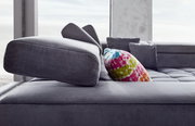 Nahaufnahme einer modernen Polsterrundecke in Grau mit verstellbarer Kopfstütze und buntem Kissen, seitliche Perspektive.
