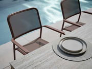 Zwei braune Stapelsessel aus Metall mit Netzgewebe, aufgestellt neben einem Pool, mit Blick von oben auf einen Tisch mit grauen Tellern.
