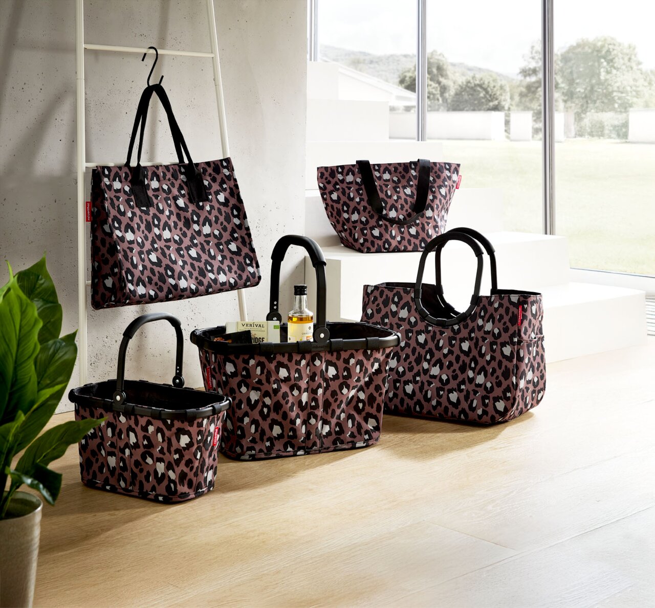 Reisenthel Carrybag Leo Chocolate Leopardenmuster-Taschenkollektion in einem modernen Raum, mit verschiedenen Größen und Formen, von vorne betrachtet.