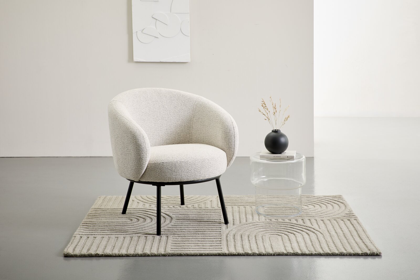 LOMOCO Sessel ODENSE Heller, gepolsterter Loungesessel in Creme/Beige mit schwarzem Metallgestell auf strukturiertem Teppich, frontale Perspektive im minimalistischen Wohnraum neben transparentem Beistelltisch mit schwarzer Vase.