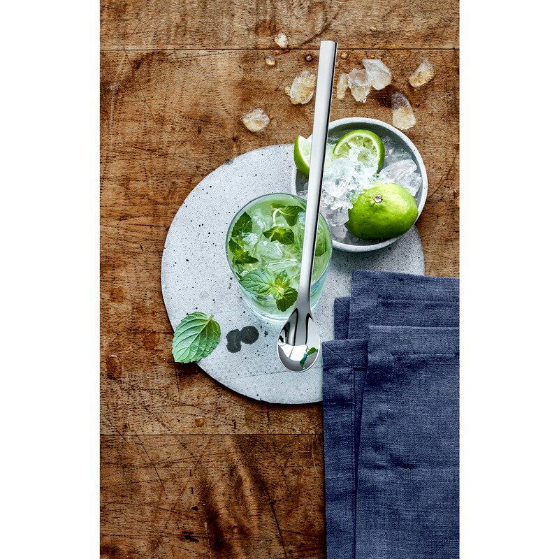 Ein eleganter Longdrinklöffel aus Edelstahl liegt auf einem Tisch neben einem Glas mit Minzblättern und Eiswürfeln, aus der Vogelperspektive betrachtet.