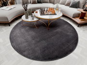 Runder, dunkelgrauer Uni-Teppich in einem modernen Wohnzimmer, von oben betrachtet, mit einem eleganten Couchtisch und einem Schachspiel darauf.
