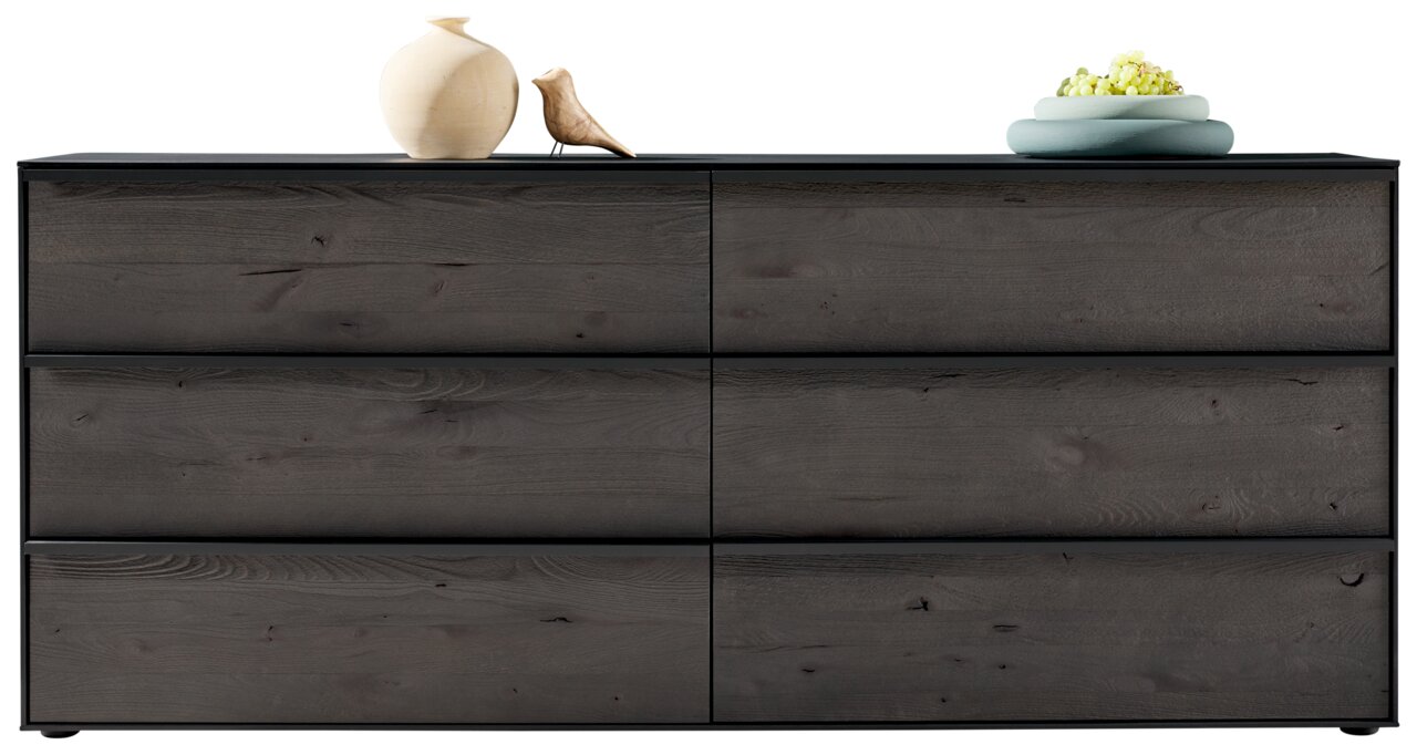 Frontale Ansicht eines modernen Sideboards mit sechs Schubladen in dunkler Holzoptik, dekoriert mit einer Vase, einer kleinen Skulptur und einer Schale mit Blumen.