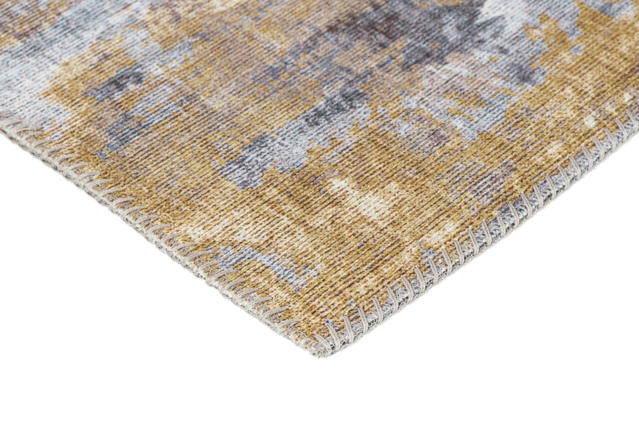 Nahaufnahme einer Ecke eines Teppichs mit abstraktem Muster in Beige- und Grautönen, perspektivisch von der Seite aufgenommen.