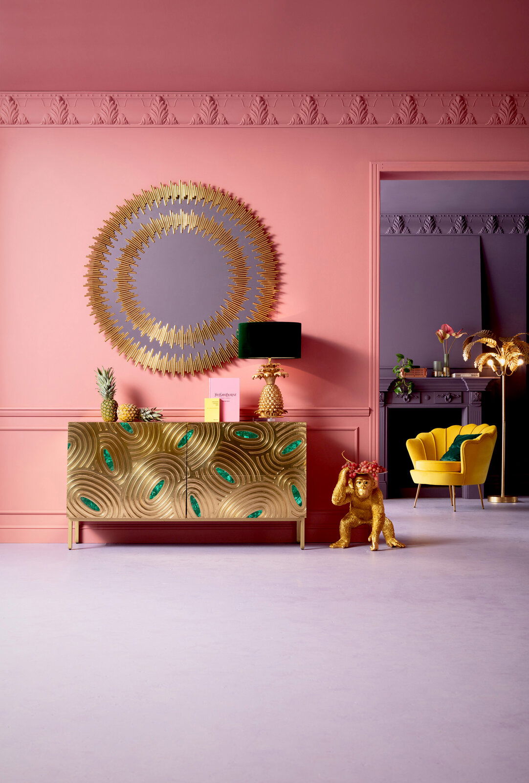 Goldene Deko-Figur eines Affen als Butler, der eine Schale mit Früchten trägt, in einem stilvoll eingerichteten Raum mit rosa Wänden und goldenen Akzenten. Perspektive: Frontalansicht.