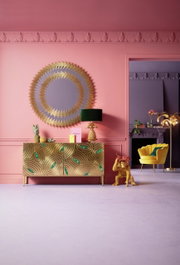 Goldene Deko-Figur eines Affen als Butler, der eine Schale mit Früchten trägt, in einem stilvoll eingerichteten Raum mit rosa Wänden und goldenen Akzenten. Perspektive: Frontalansicht.